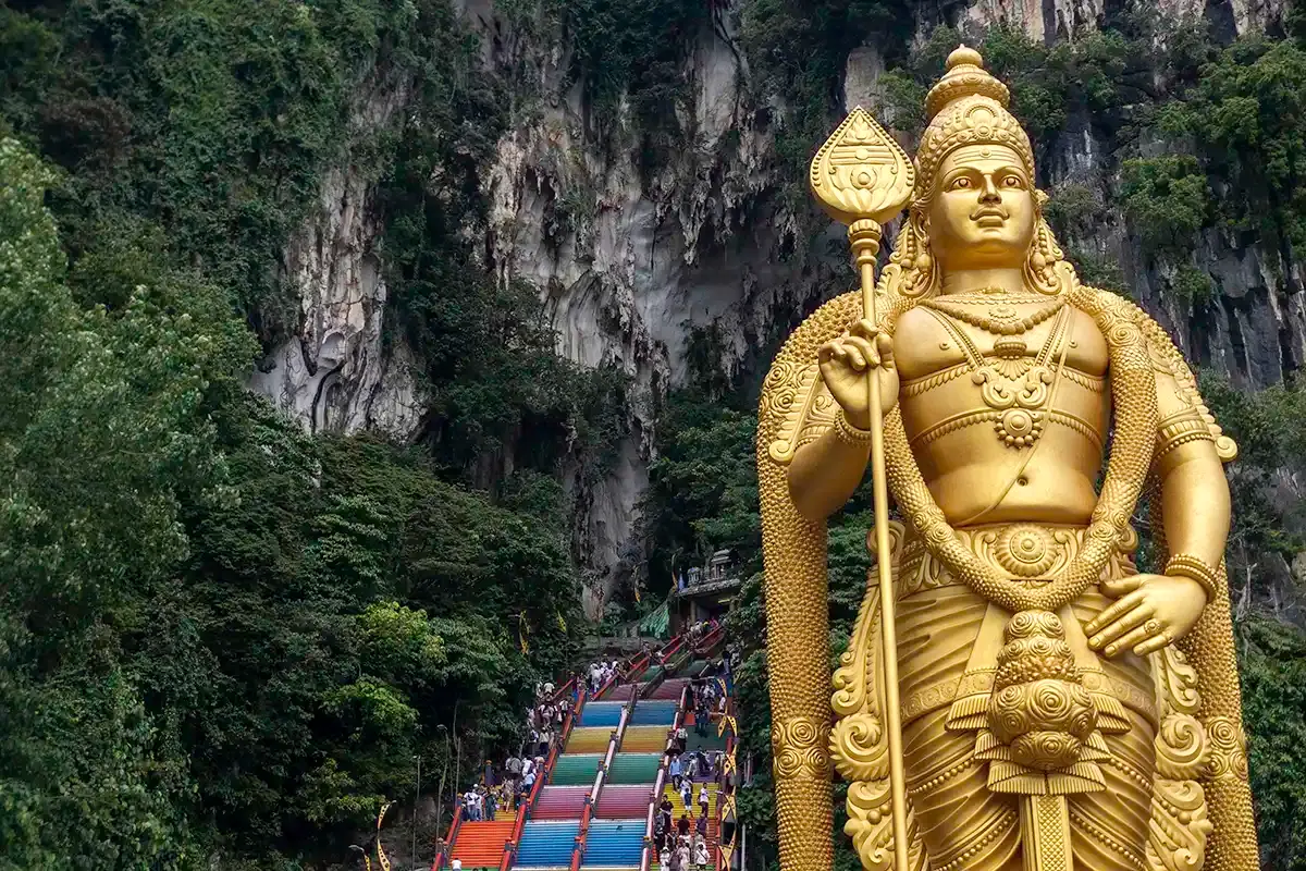 Golden Lord Murugan statue beside the colourful staircase leading to the Batu Caves temple in Selangor, Malaysia.