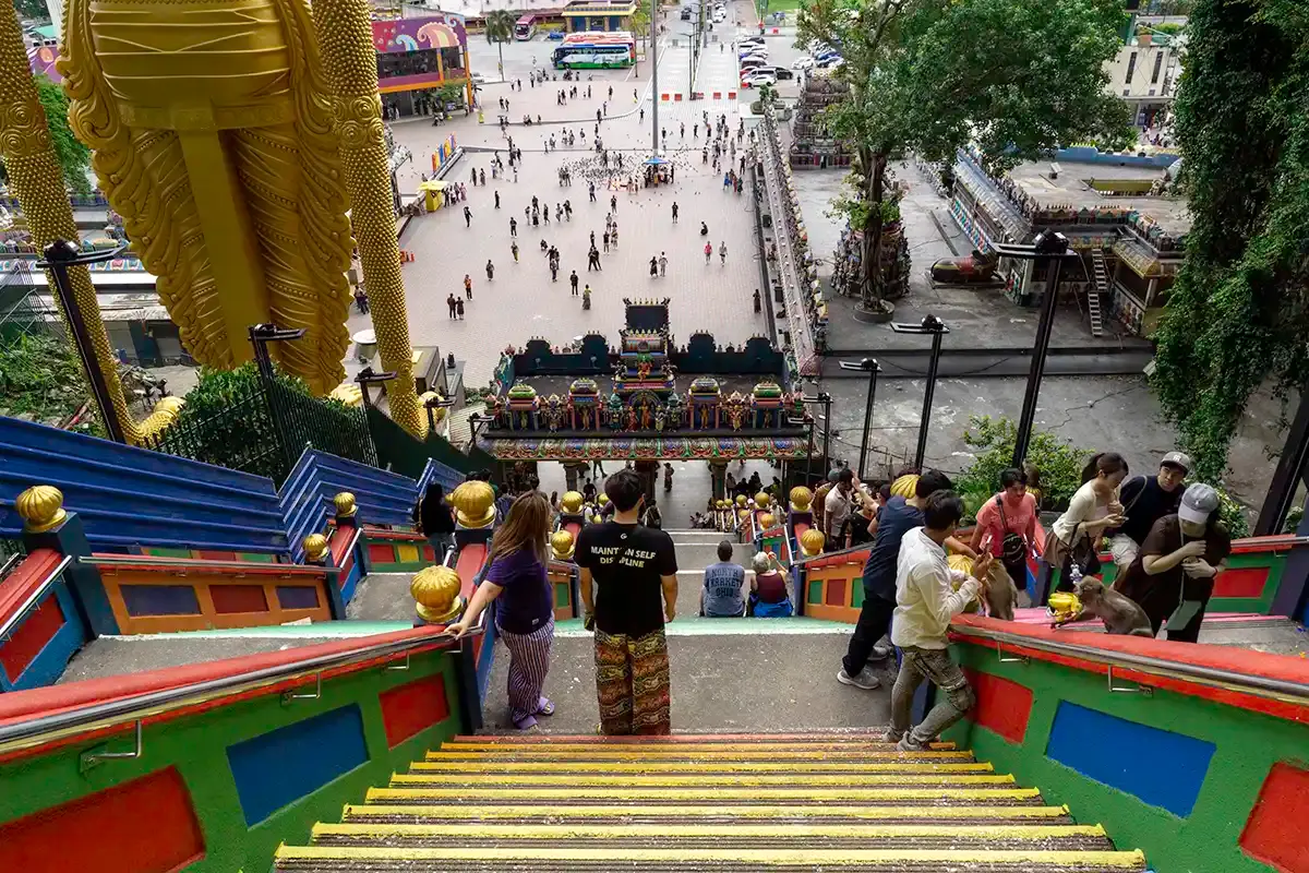 View from the top of Batu Caves staircase looking down towards the temple entrance and visitor plaza in Selangor, Malaysia.