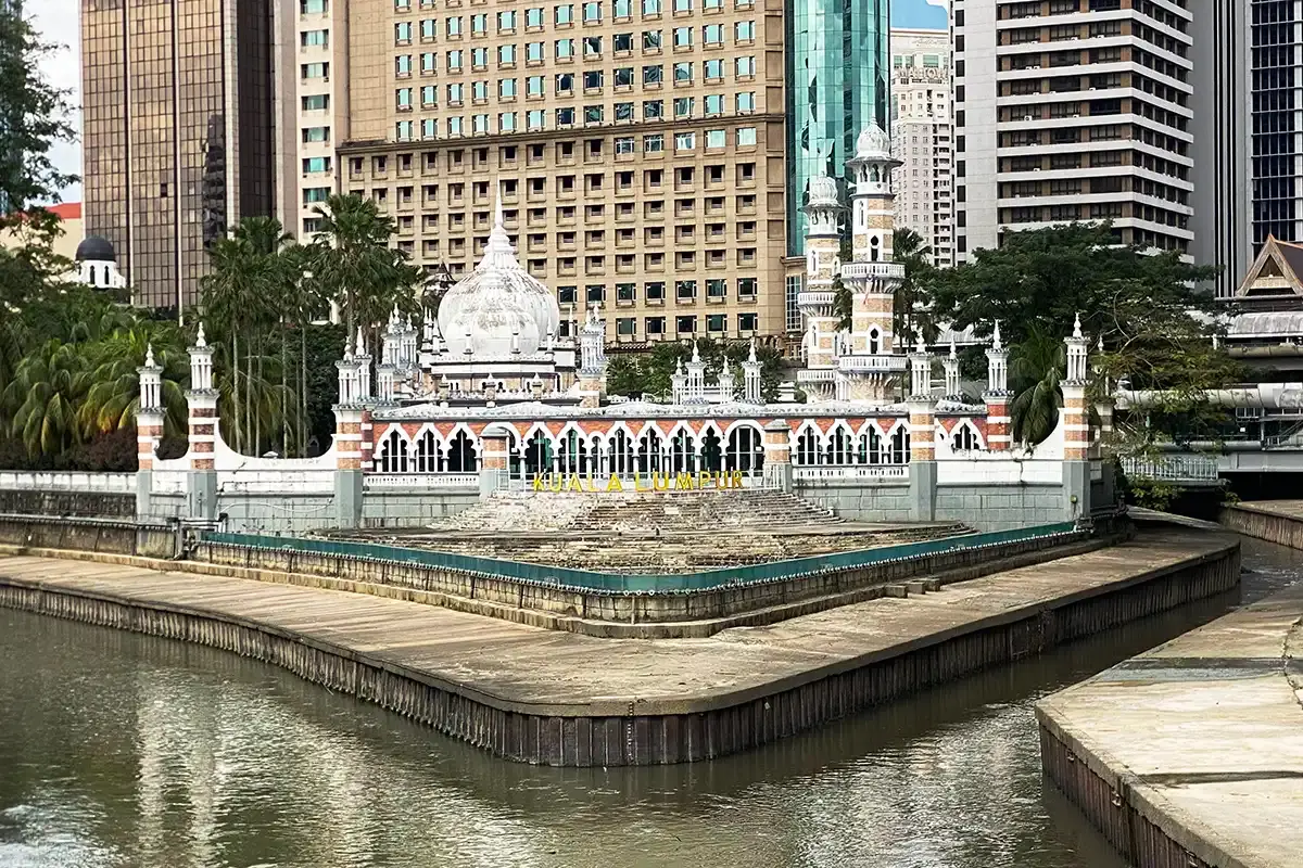 Masjid Jamek in central Kuala Lumpur, seen beside the river with surrounding city buildings in the historic city centre.