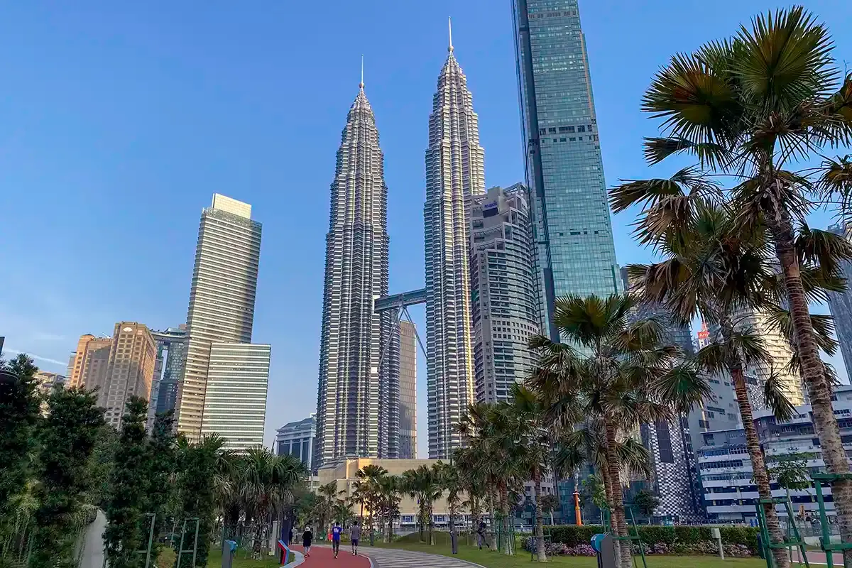 Petronas Twin Towers viewed from KLCC Park in Kuala Lumpur, with the surrounding skyline and palm trees in the foreground.
