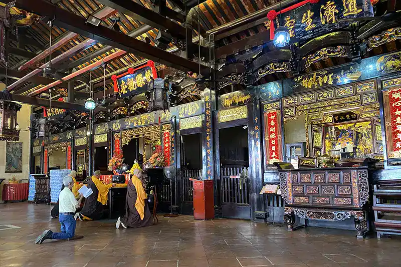 Inside Cheng Hoon Teng Temple in Malacca with monks and visitors praying during a cultural day trips from Kuala Lumpur.