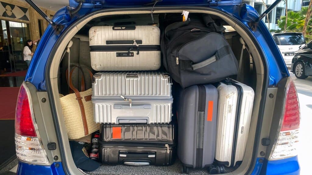 Suitcases and bags loaded into the boot of a blue Toyota Innova MPV at a Kuala Lumpur hotel entrance before a private transfer